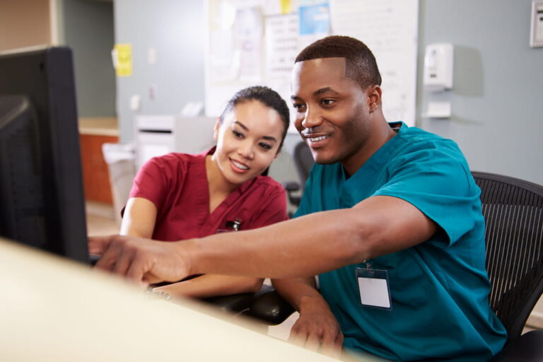 Female and male nurses at workstation viewing desktop computer