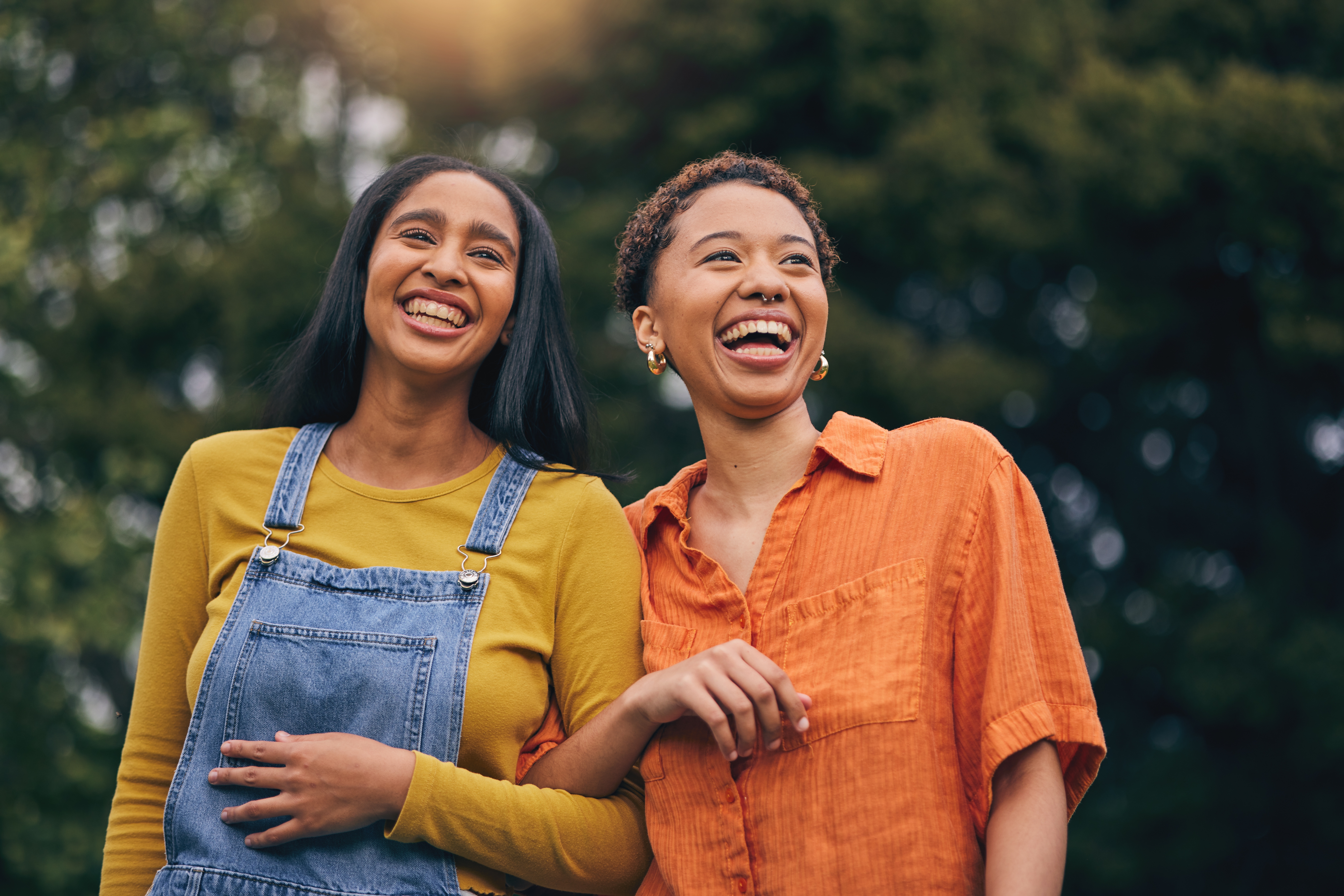 Two young friends walking in the park arm-in-arm laughing