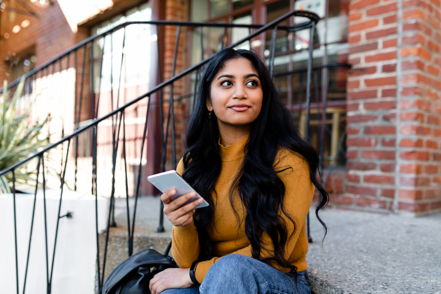 Beautiful young woman sits outdoors on steps and checks her smartphone.