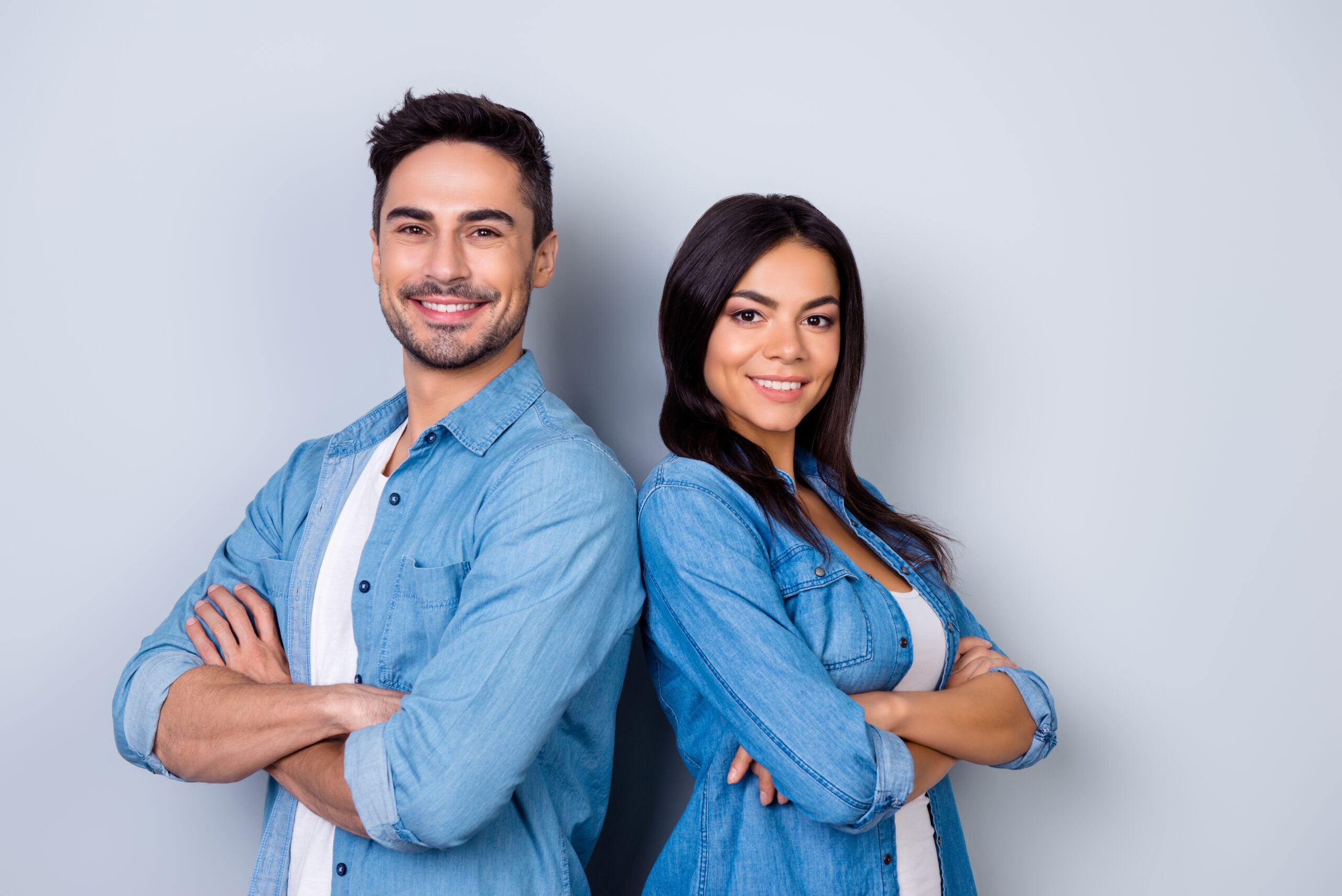 Happy man and woman standing back to back with arms crossed