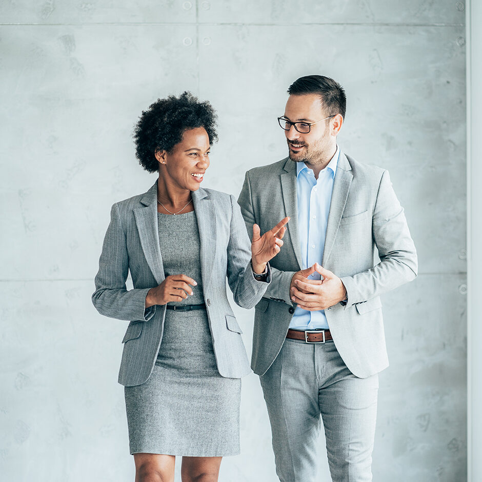 Two smiling business people walking through office hall and talking
