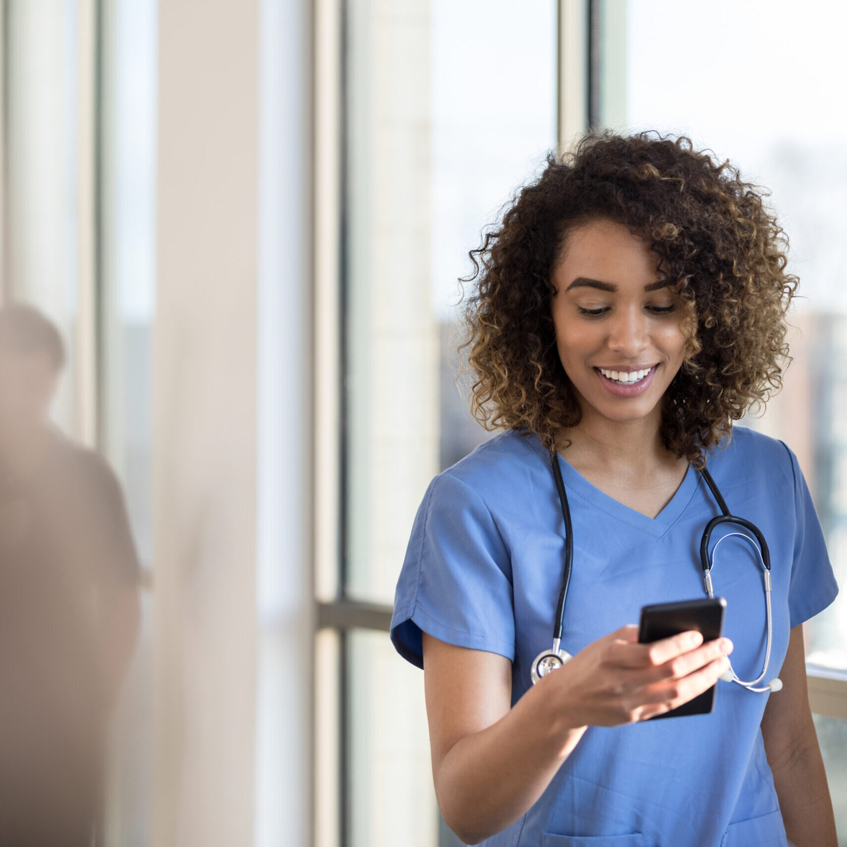 Attractive young female nurse checks smartphone as she walks in a hospital hallway