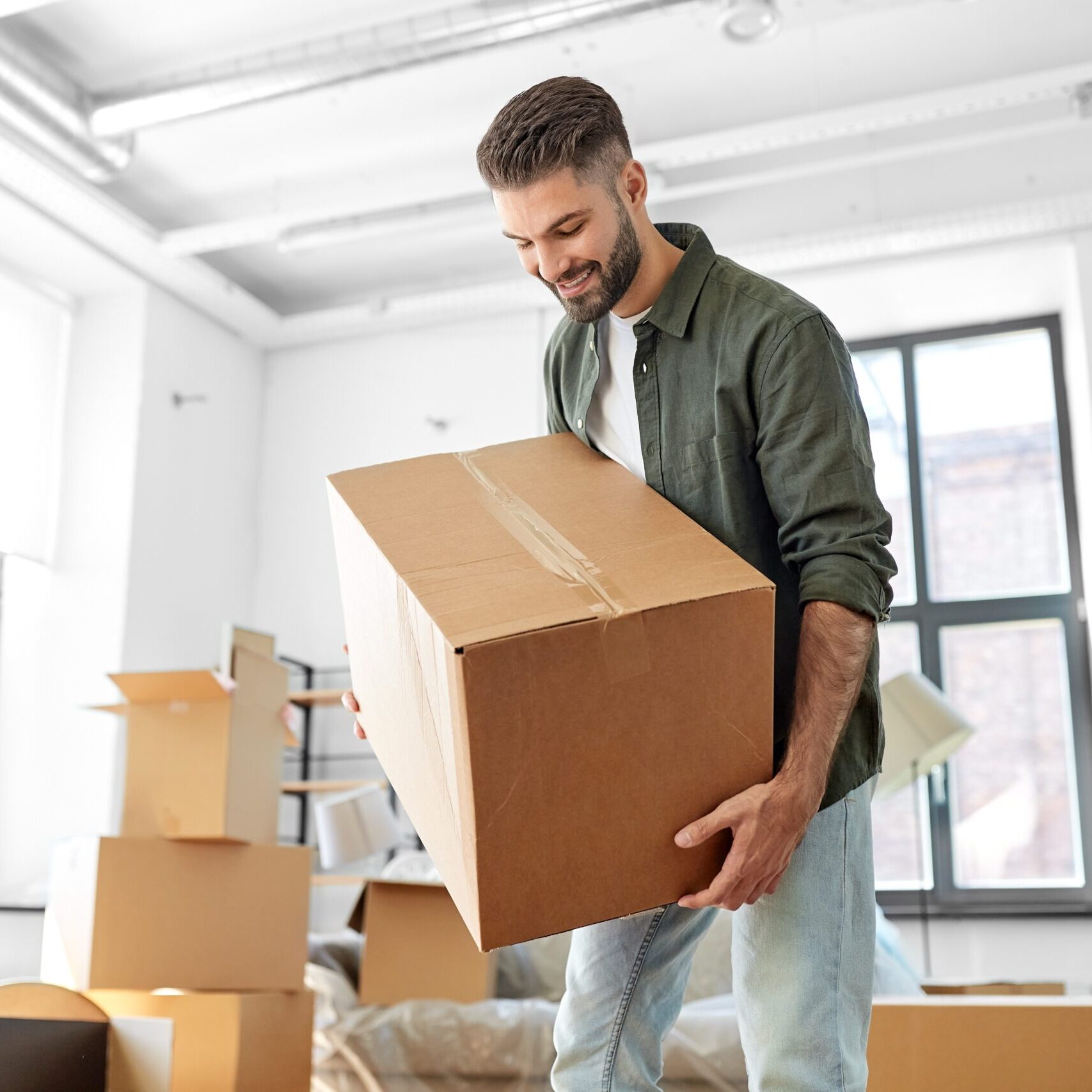 Happy smiling young man carrying moving box into new home